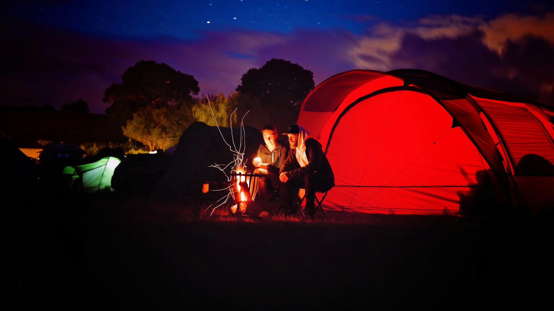 man and woman sitting beside bonfire during nigh time