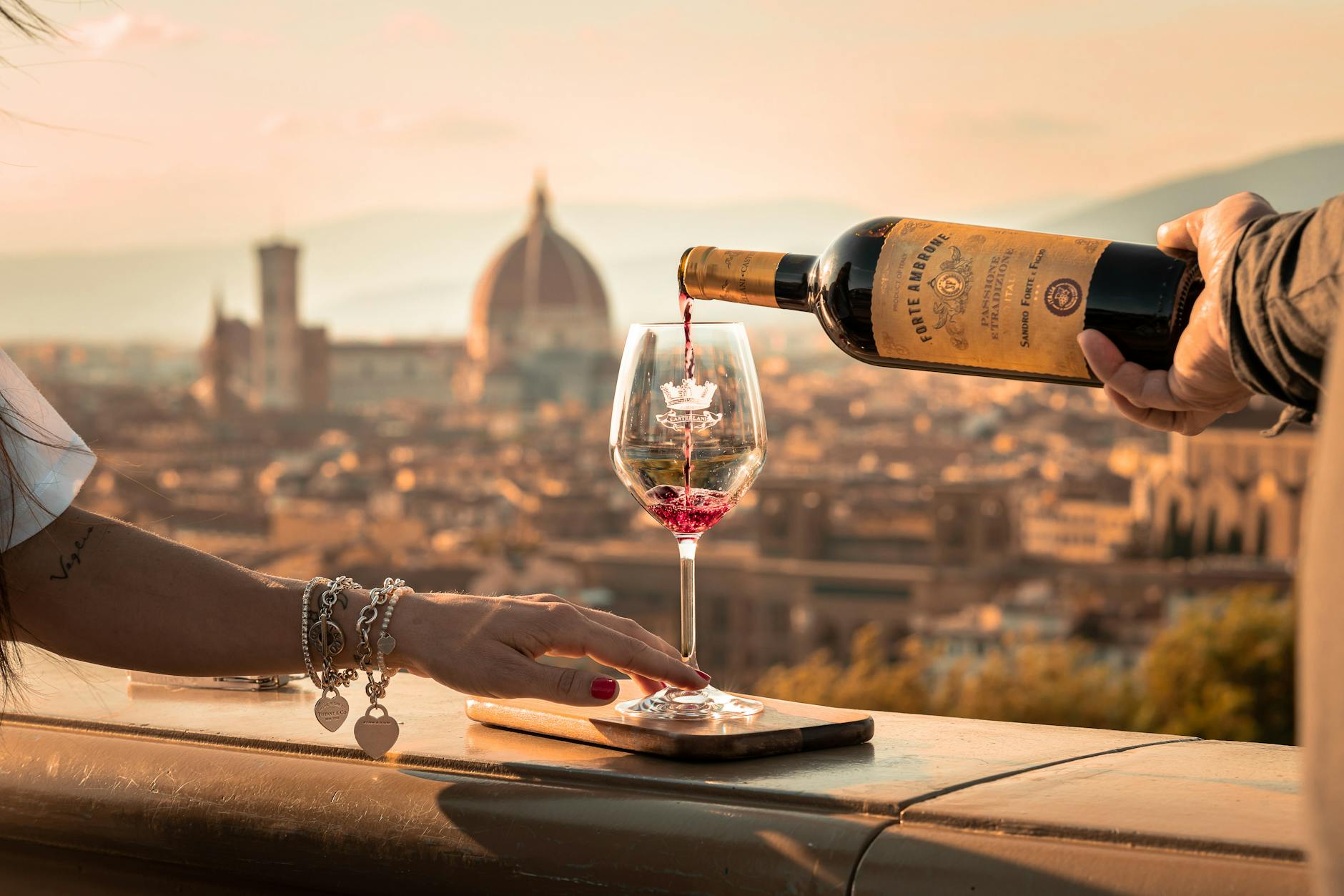 pouring wine to woman glass in sunlight and with town behind