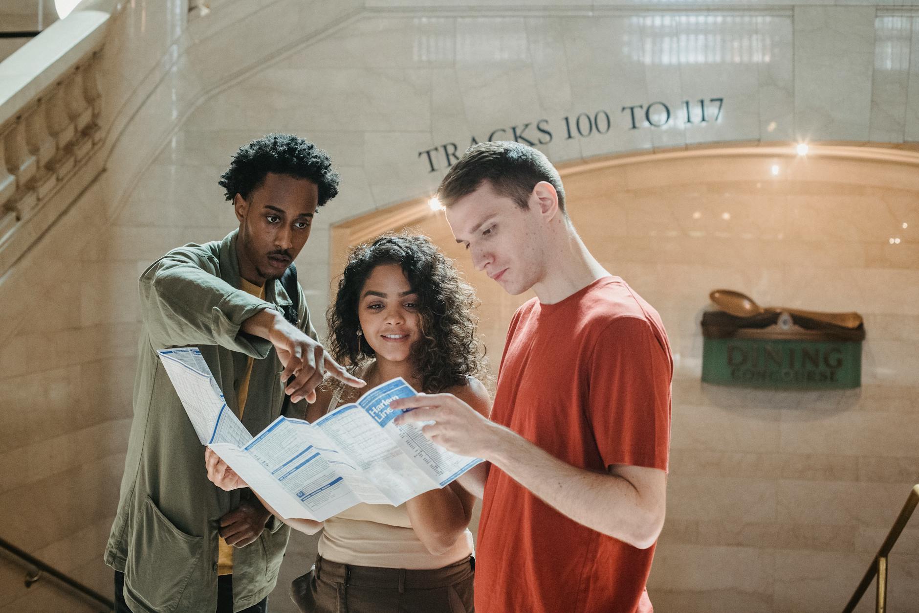young focused diverse students exploring map in railway station