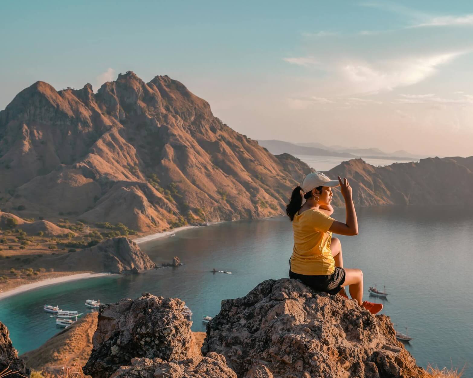 woman making peace hand sign while sitting on rock boulder
