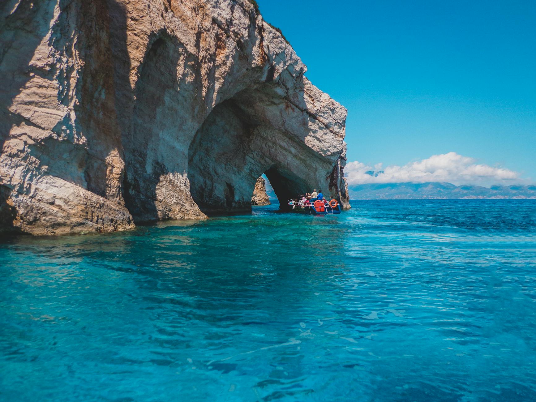 people riding on boat near the rock formation under the blue sky