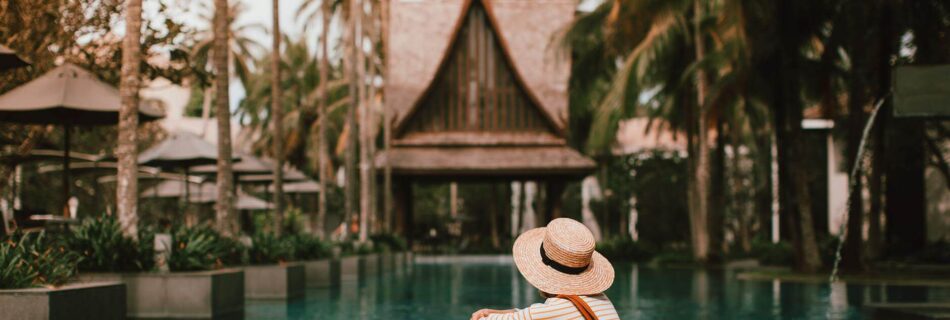 woman in hat with bag resting near turquoise pond