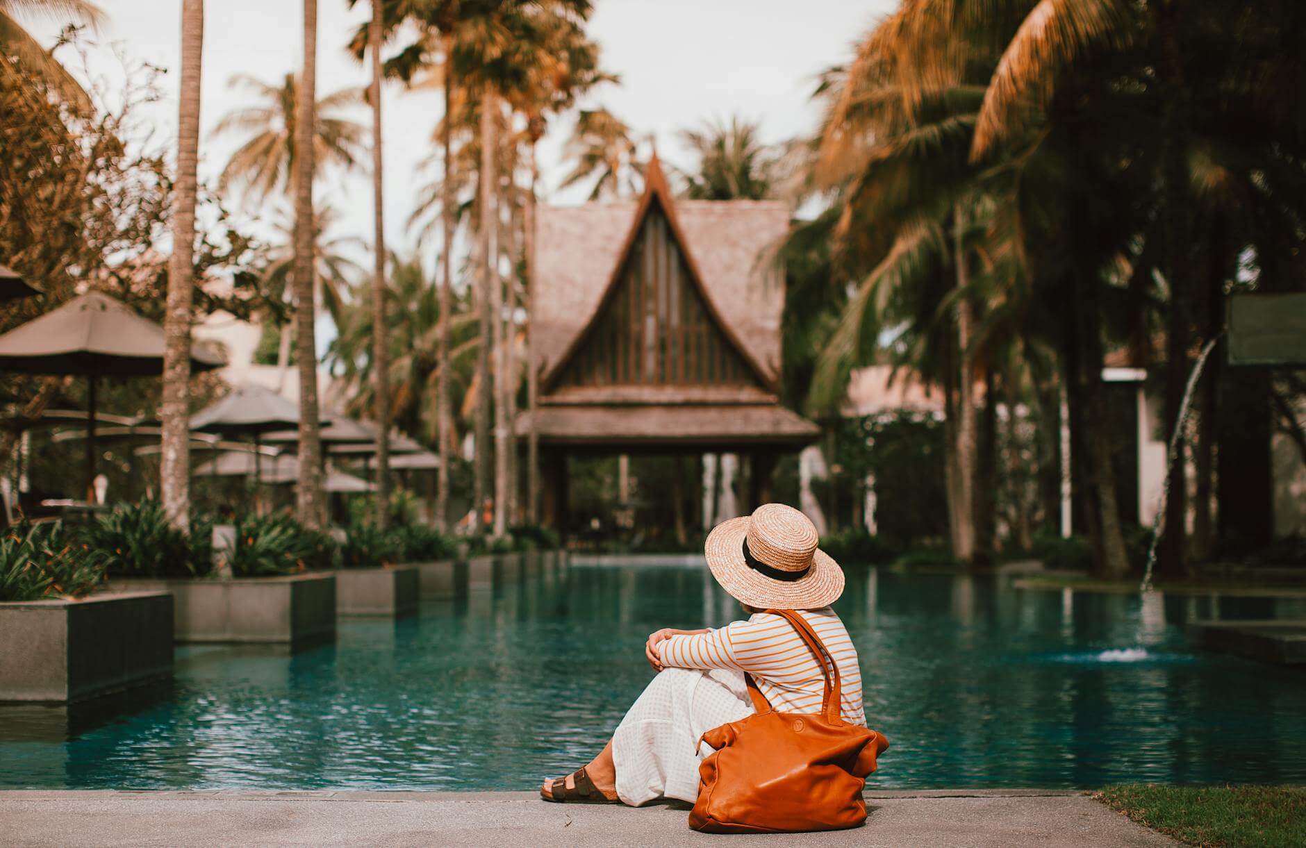 woman in hat with bag resting near turquoise pond